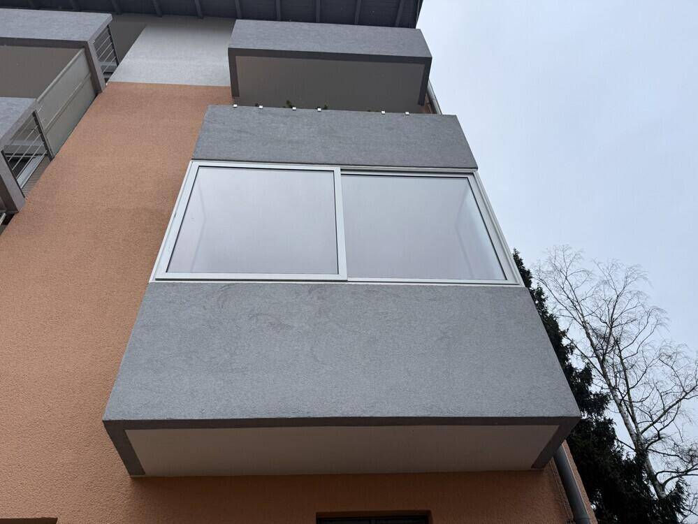 Nahaufnahme einer verglasten Loggia am Apartmentgebäude mit Blick auf die Umgebung.