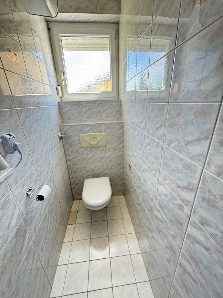 Kleines, gefliestes WC mit Toilette und einem Fenster für natürliche Belüftung und Licht.