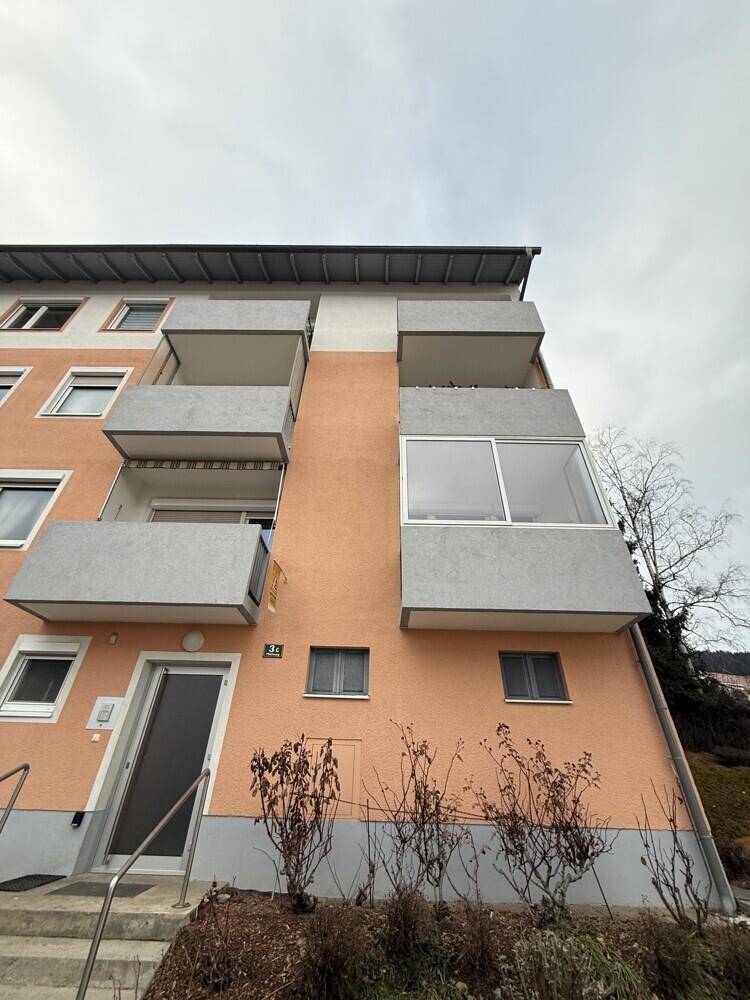 Vorderansicht eines Apartmentgebäudes mit mehreren Balkonen und einer Fassade in Pfirsich- und Grautönen.