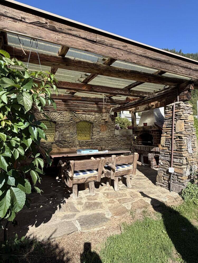 Überdachter Grillplatz mit Steintisch, Holzbänken und rustikalem Mauerwerk.