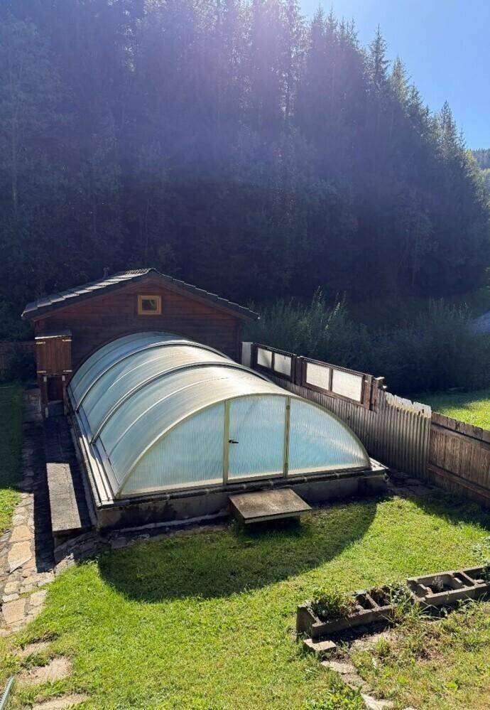 Überdachter Swimmingpool im Garten, umgeben von Grünflächen und Bäumen.