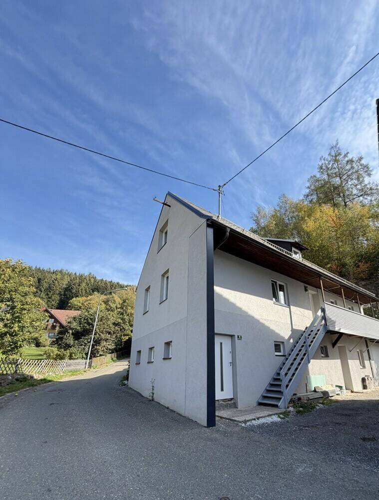 Ansicht des Hauses mit Eingangstür und Außentreppe, umgeben von grüner Landschaft.