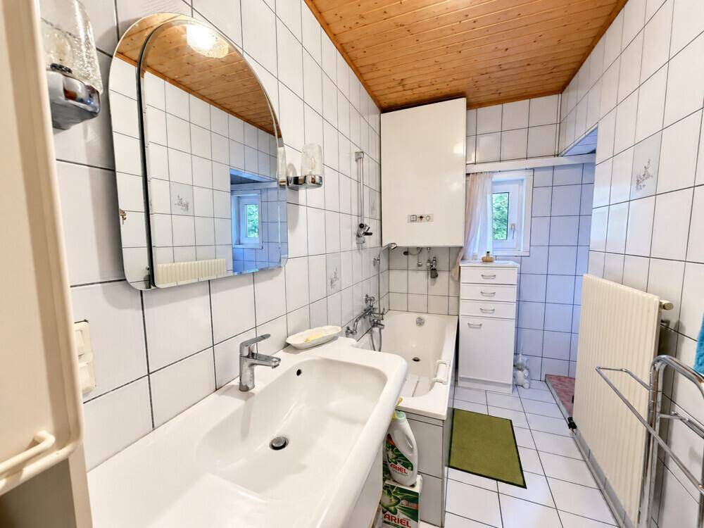 Badezimmer mit Waschbecken, Spiegel, Badewanne und weißen Wandfliesen.