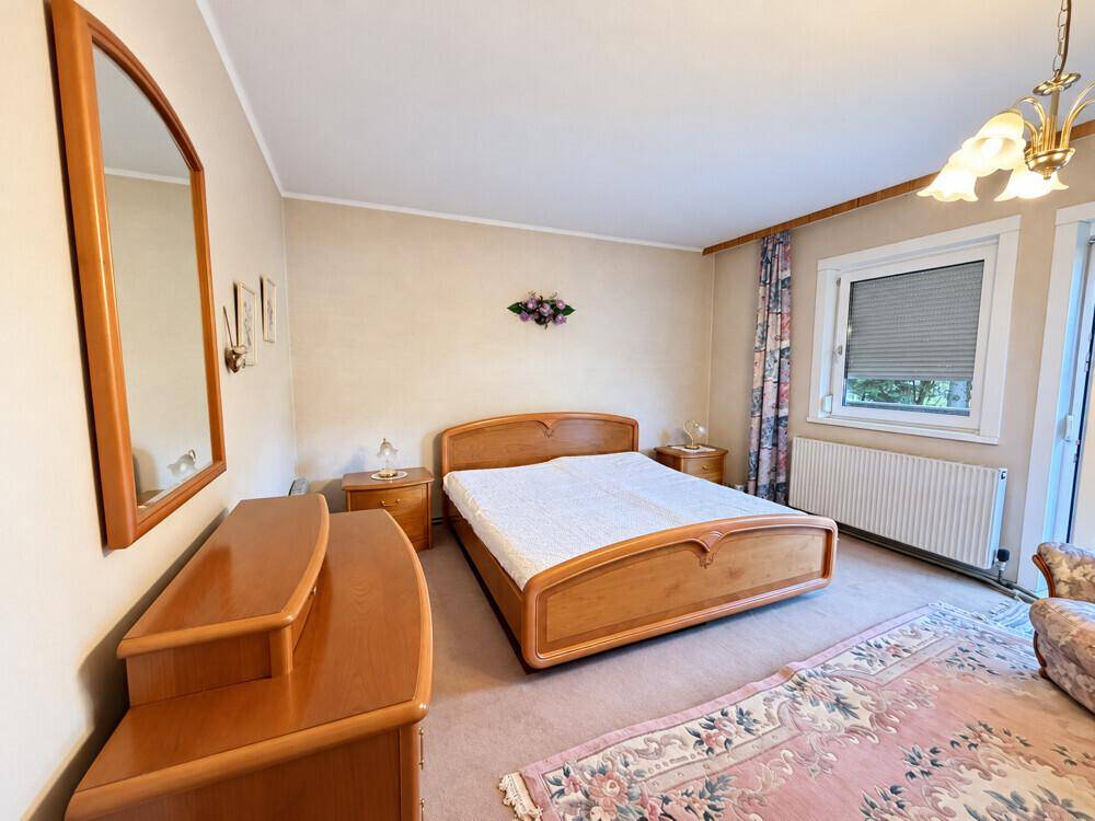 Schlafzimmer mit klassischem Holzbett, Nachttischen, Kommode und Teppichboden.