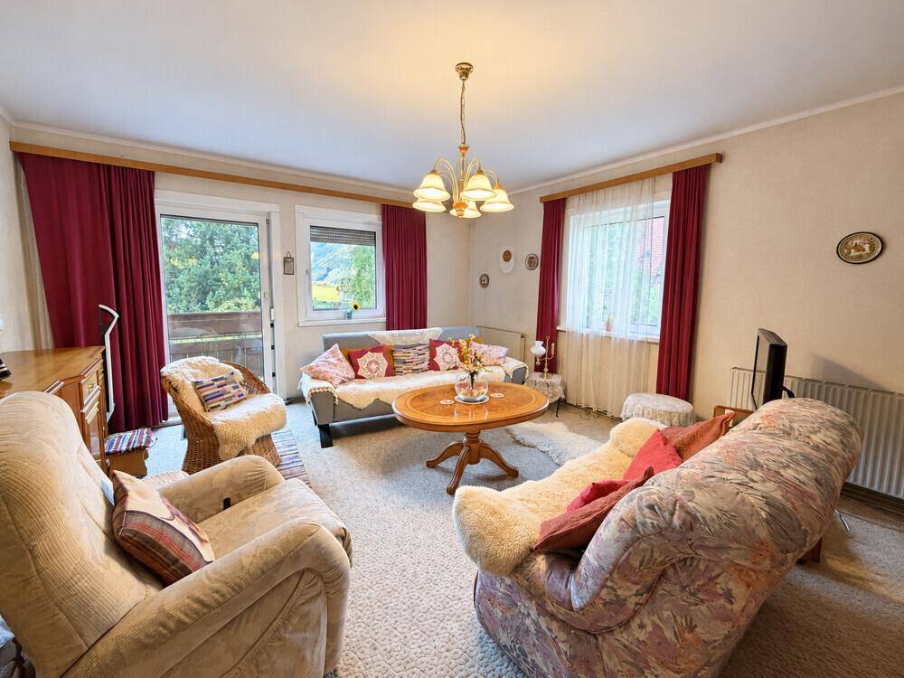Helles Wohnzimmer mit bequemen Sofas, Teppichboden und Zugang zu einem Balkon mit Aussicht.
