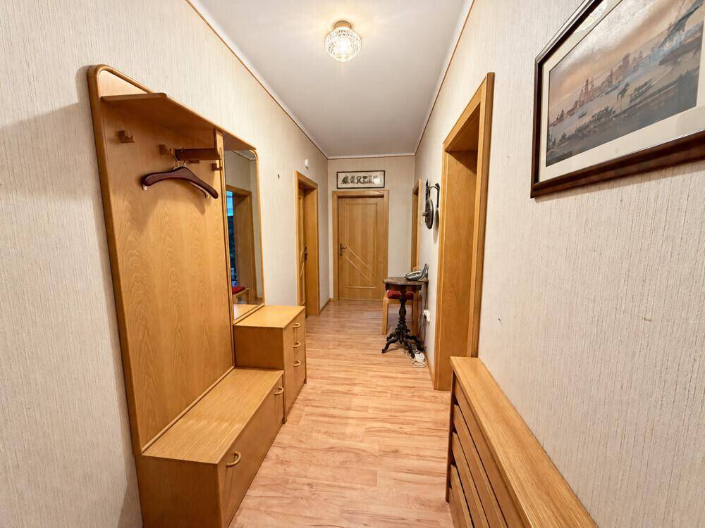 Heller Flur mit Holzgarderobe, Spiegel und Laminatboden, der zu weiteren Räumen führt.