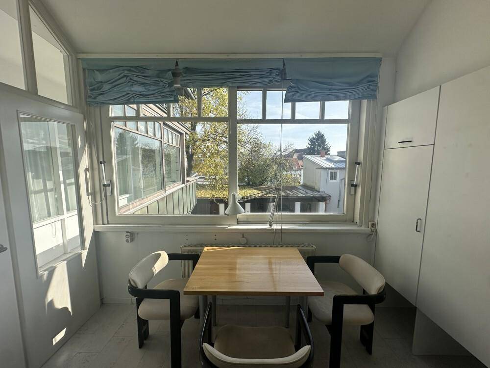 Heller Essbereich in einem Wintergarten mit großen Fenstern und Blick ins Grüne.