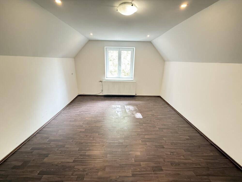 Helles Zimmer im Dachgeschoss mit dunklem Laminatboden, weißen Wänden und Dachschrägen.