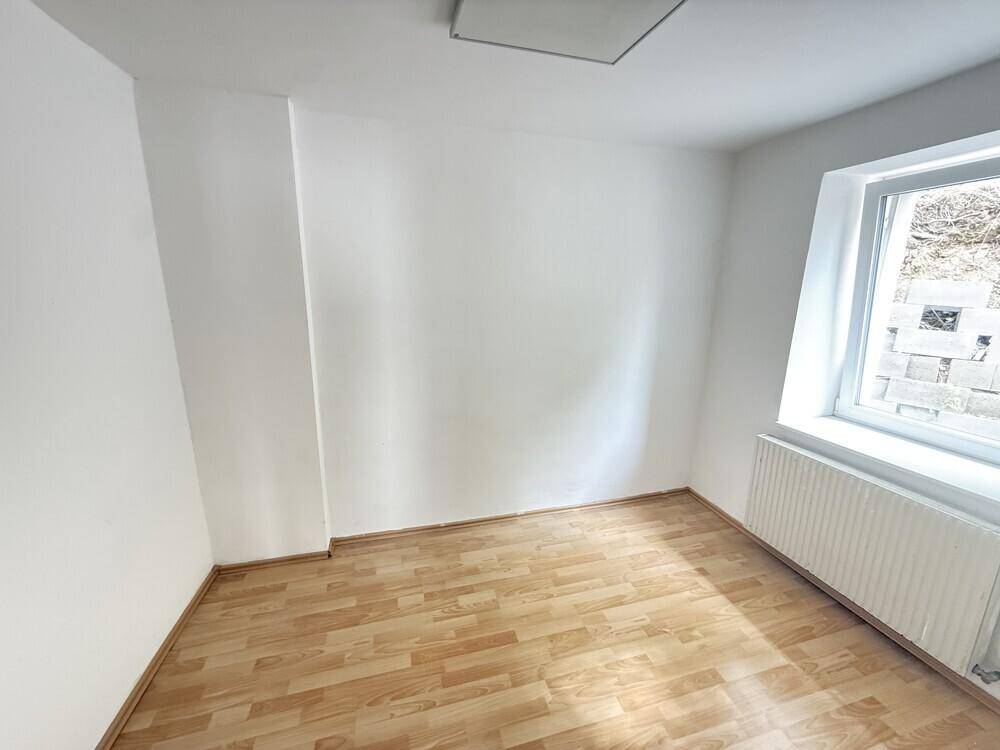 Gemütliches Schlafzimmer mit Laminatboden, weißen Wänden und einem Fenster, ausgestattet mit Heizkörper.