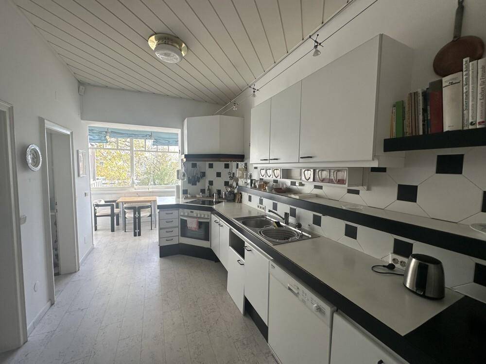 Geräumige Küche mit weißen Schränken, schwarzen Arbeitsplatten und einem Essbereich am Fenster.