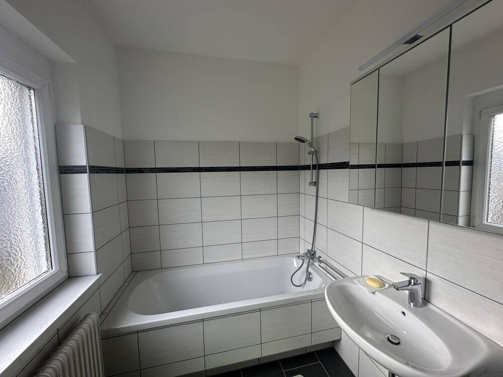 Badezimmer mit Badewanne, Waschbecken, Spiegelschrank und Fenster für Tageslicht.