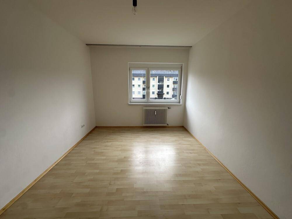 Helles Schlafzimmer mit Laminatboden und einem Fenster mit Blick auf die Umgebung.