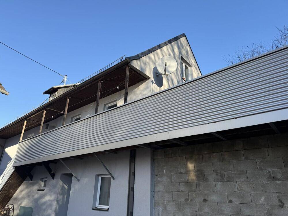 Nahaufnahme des Balkons und des Daches eines Hauses unter strahlend blauem Himmel.