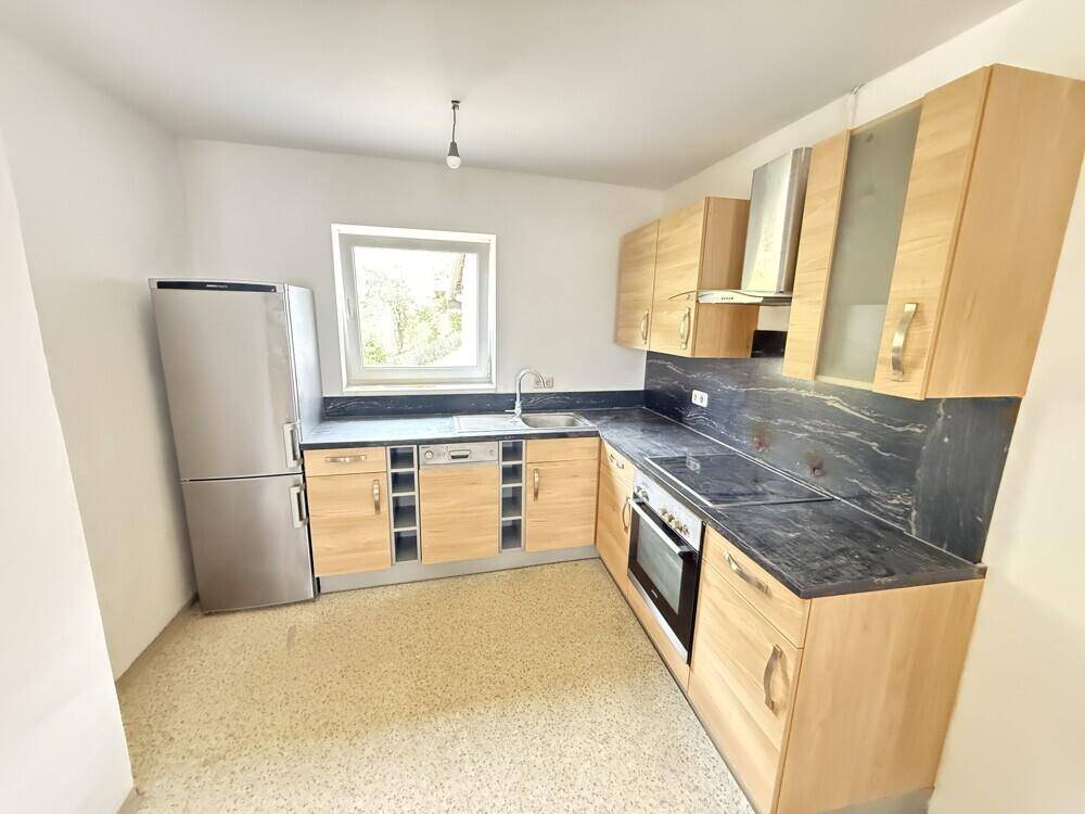 Funktionale Küche mit Holzschränken, dunklen Arbeitsplatten und modernen Geräten, inklusive Fenster.