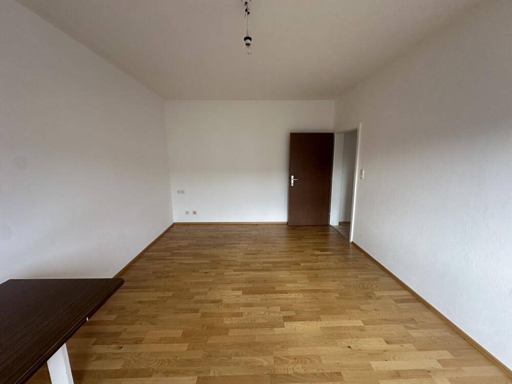 Leeres Wohnzimmer mit Laminatboden und einer Holztür, bereit zur individuellen Gestaltung.