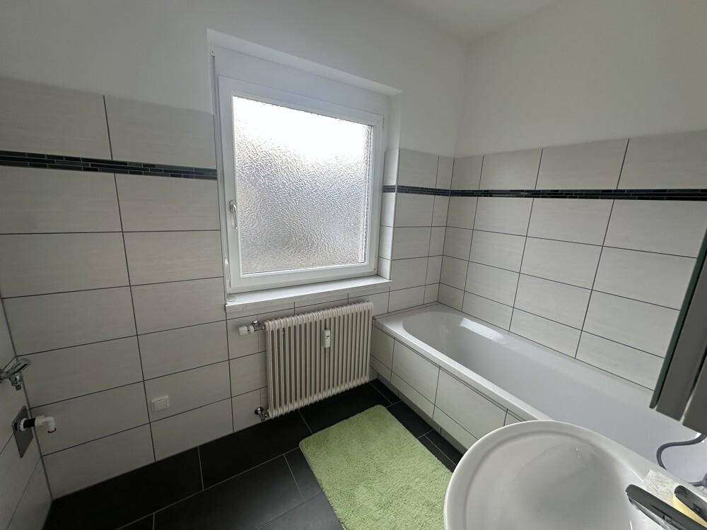 Helles Badezimmer mit Badewanne, Fenster und Fliesen in Weiß und Schwarz.