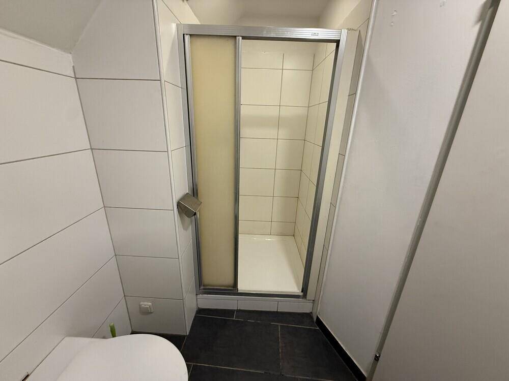 Badezimmer mit Duschkabine, dunklem Fliesenboden und Dachschräge, bietet eine praktische Raumnutzung.
