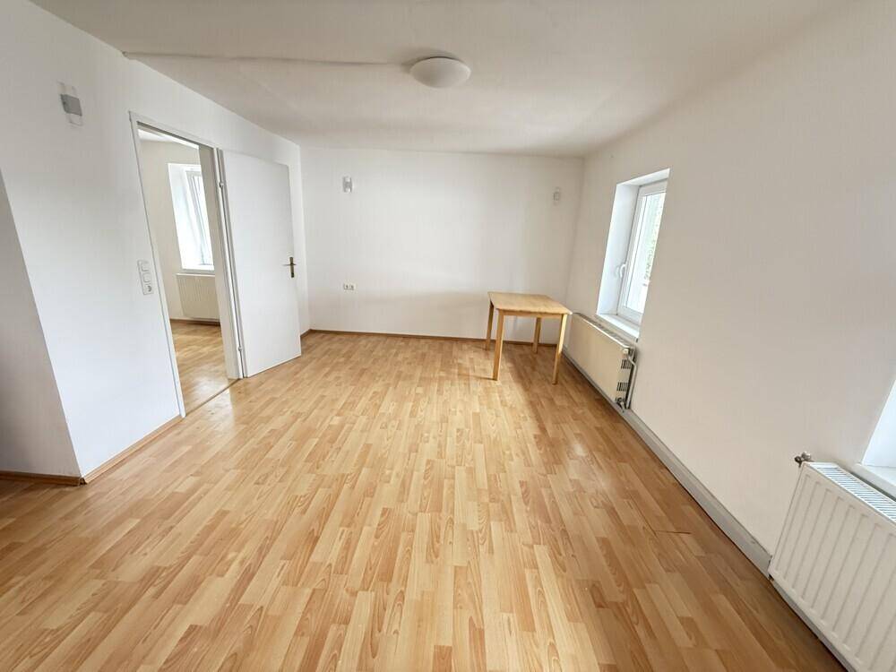 Helles Zimmer mit Laminatboden, weißen Wänden und zwei Fenstern, ideal als Wohn- oder Schlafzimmer.