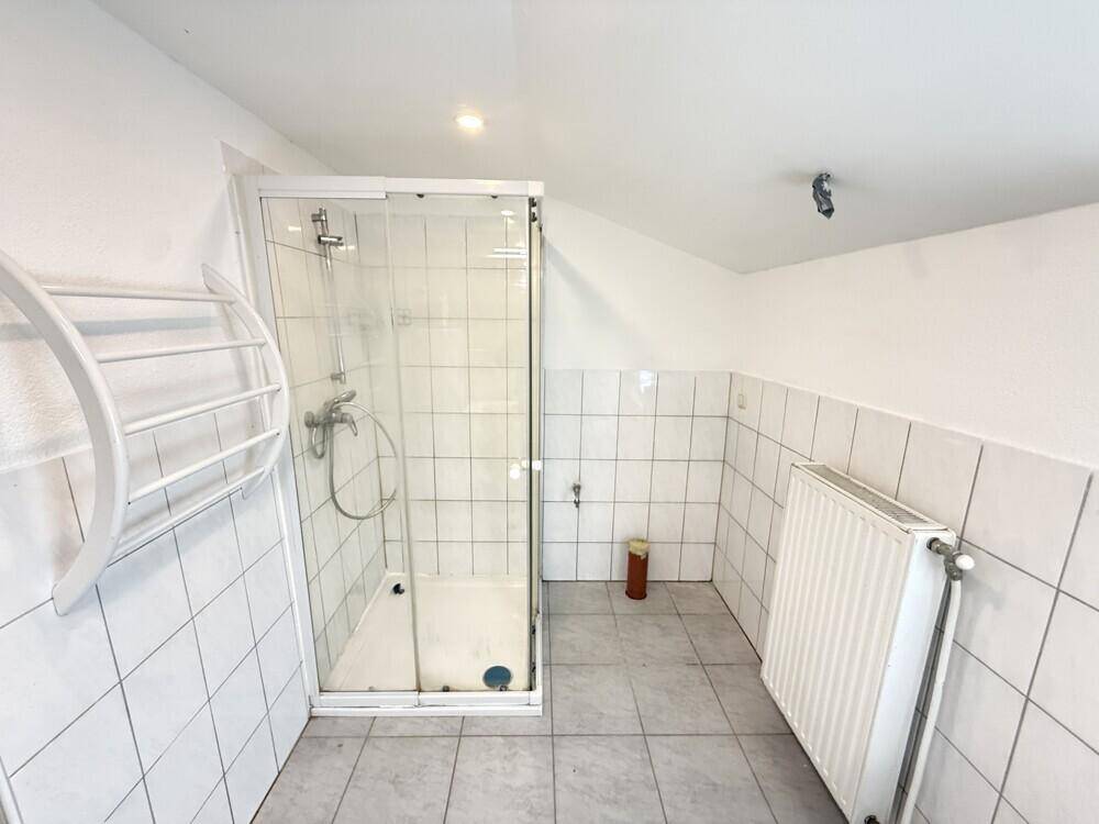 Badezimmer mit Duschkabine, weißen Fliesen an Wänden und Boden sowie einem Heizkörper.