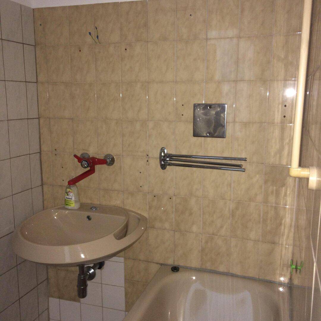 Badezimmer mit beigefarbenen Fliesen, Waschbecken und Badewanne in älterem Stil.