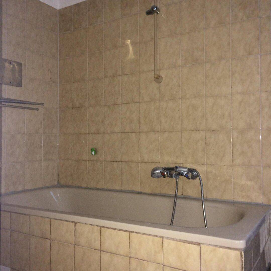 Badezimmer mit beigefarbenen Wandfliesen und einer Badewanne mit Duschvorrichtung.