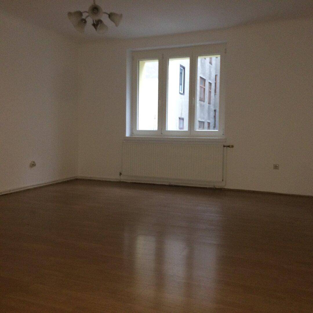 Leerer Raum mit Holzfußboden und Fenster, das auf ein gegenüberliegendes Gebäude blickt.
