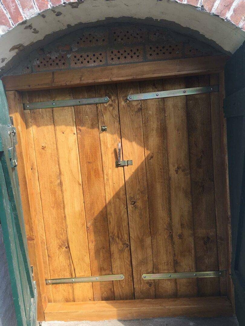 Robuste Holztüren mit Metallbeschlägen in einem gemauerten Torbogen.