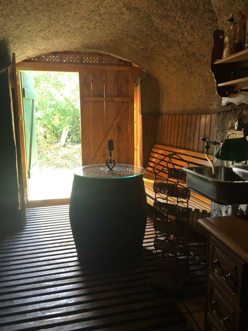 Heller Weinkeller mit Holzboden, Fass als Tisch und offenem Ausgang ins Grüne.