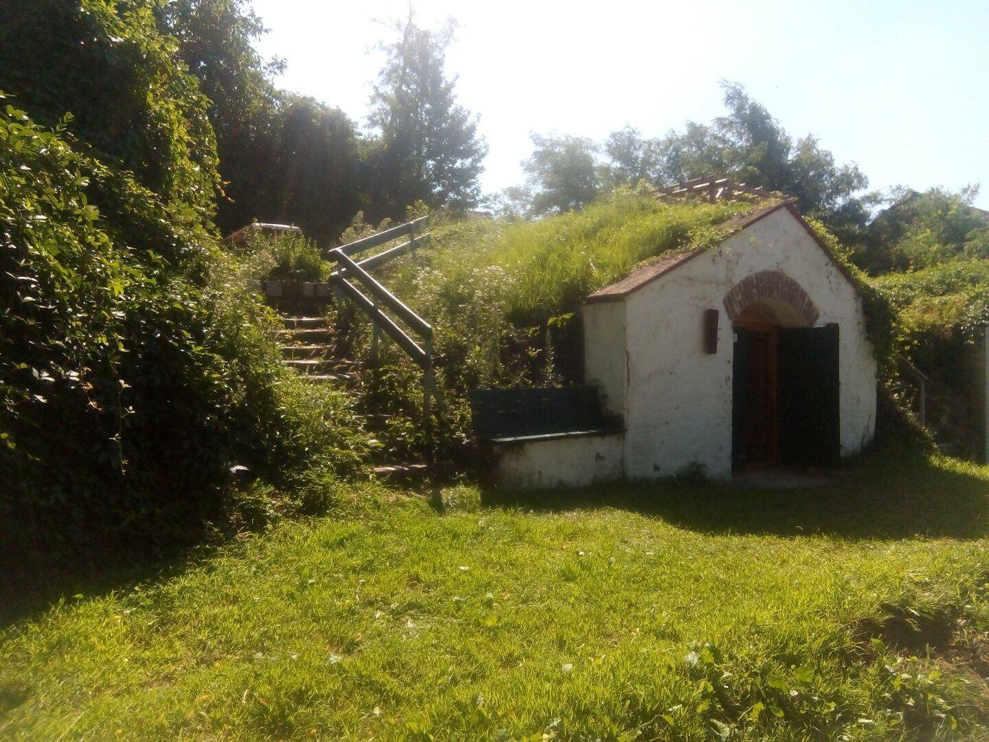 Traditionelles kleines Gebäude mit begrüntem Dach, eingebettet in einen Hügel mit Treppe.