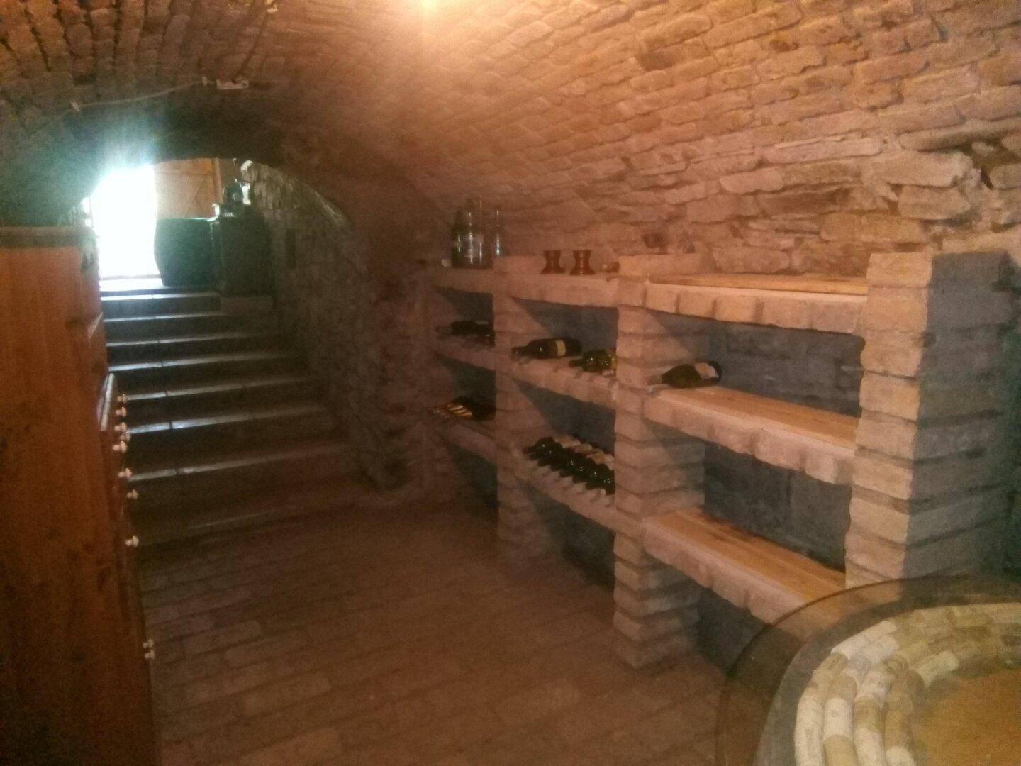 Rustikaler Weinkeller mit gemauerten Regalen, Weinflaschen und Steinstufen.