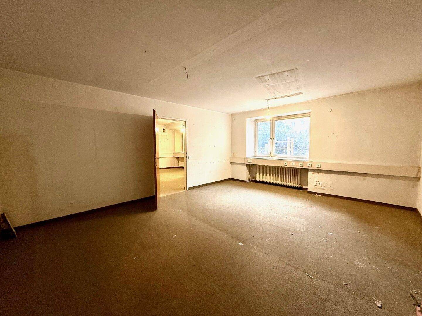 Leerer Raum mit schmutzigem Boden, einem Fenster und einfacher Ausstattung, der auf eine neue Nutzung wartet.
