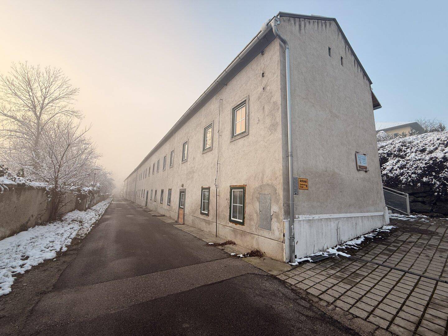 Lange Fassade eines alten Gebäudes mit vielen Fenstern entlang einer verschneiten Straße.