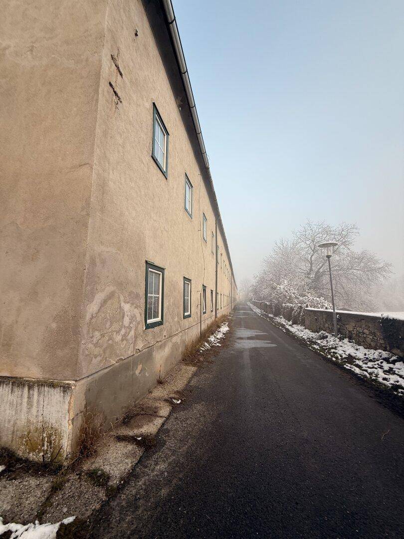 Seitenansicht eines langen Gebäudes mit Putzfassade und Fenstern an einem nebligen Wintertag.