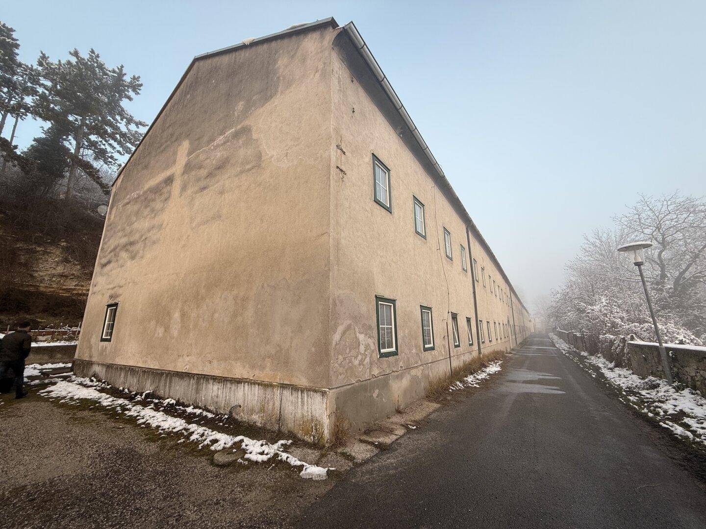 Endansicht eines langen Gebäudes mit schlichter Putzfassade und wenigen Fenstern im Winter.