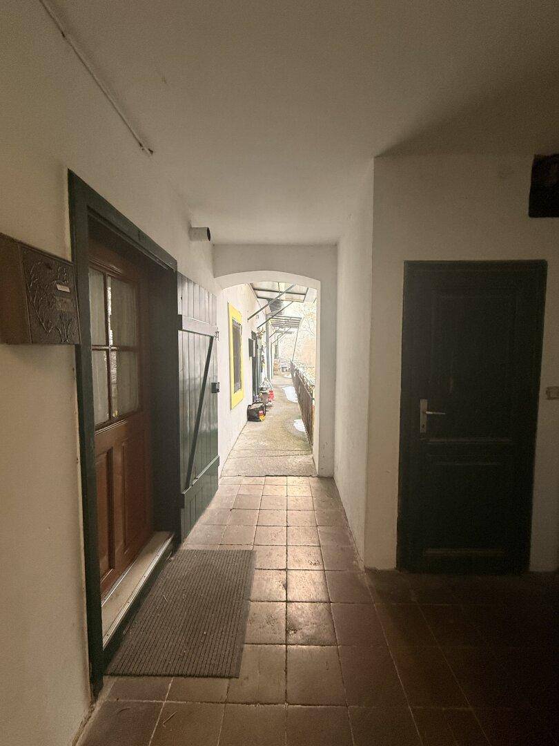 Langer, gefliester Flur mit Holztüren und Blick auf den verschneiten Außenbereich.