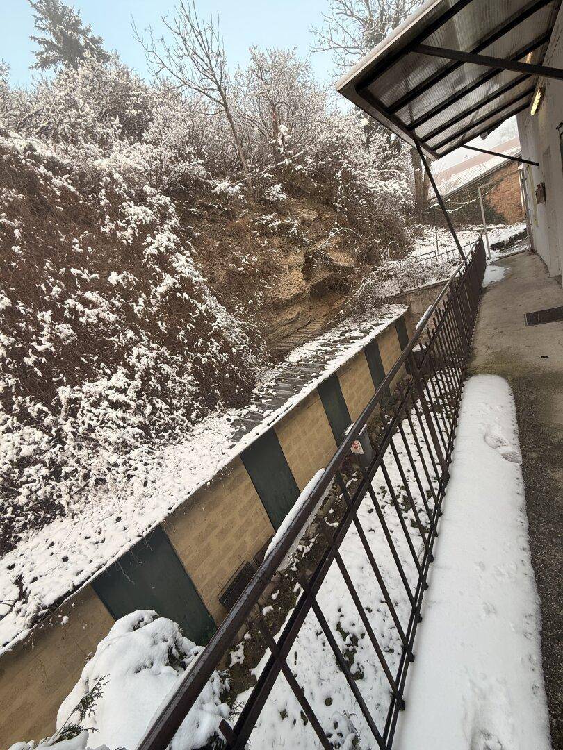 Verschneite Böschung mit einer Stützmauer und einer Treppe neben dem Gebäude.