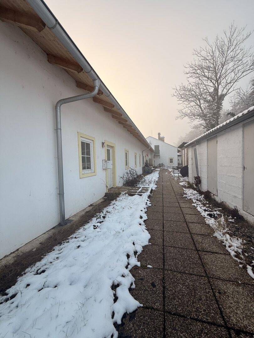 Lange Gebäudeseite mit weißer Fassade und einem gepflasterten Weg im Schnee.