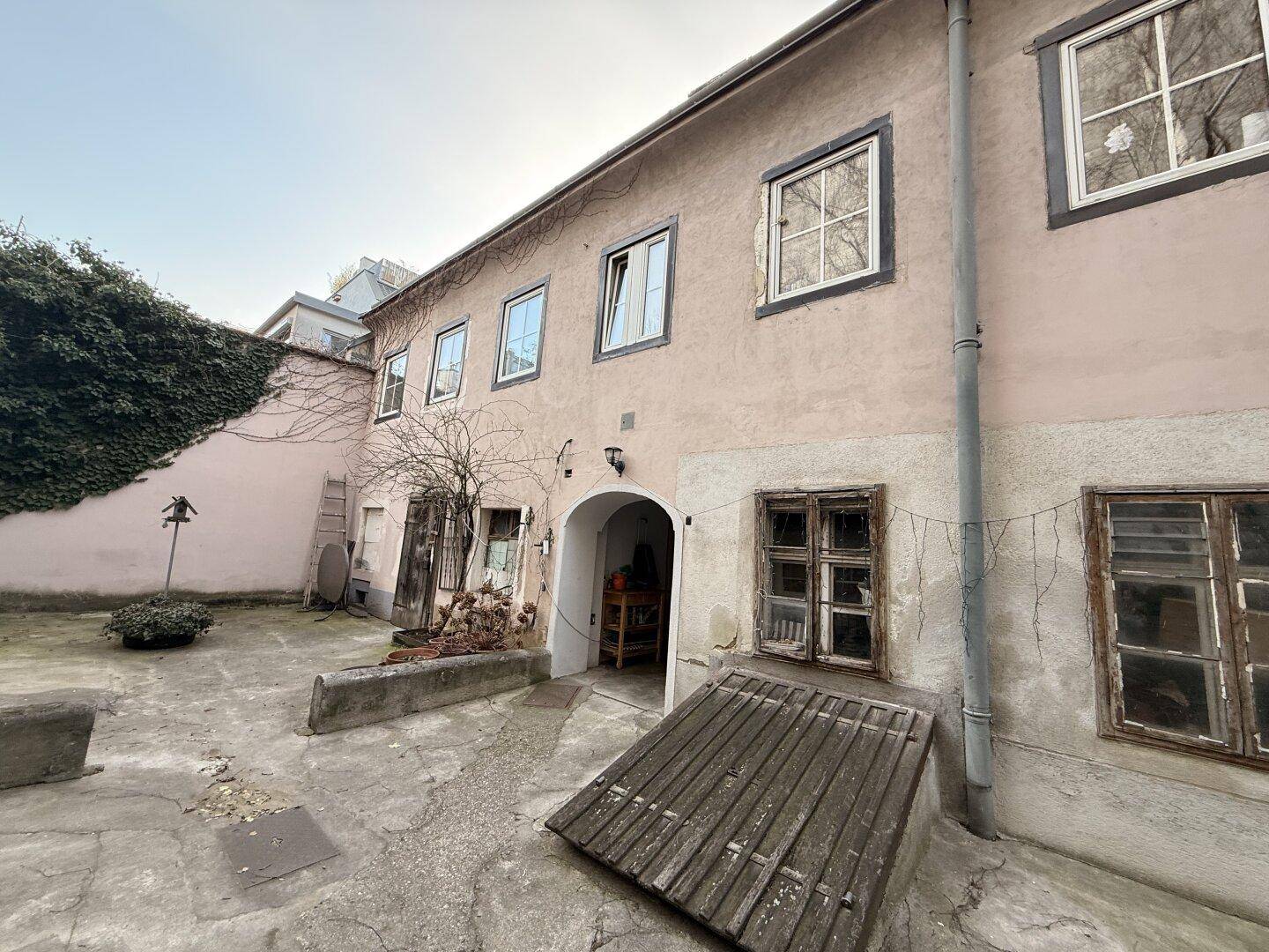 Ansicht einer Altbaufassade im Innenhof mit Fenstern und einem Zugang zum Kellerbereich.