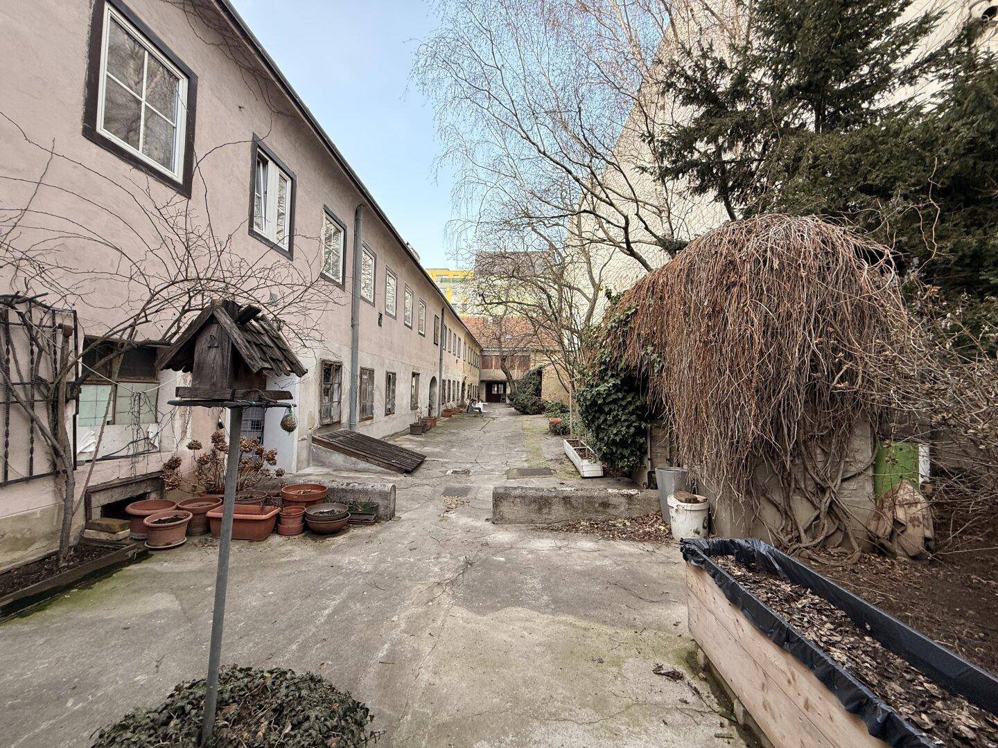 Weitläufiger Innenhof mit verschiedenen Gebäudeteilen, Bäumen und einem Vogelhaus.