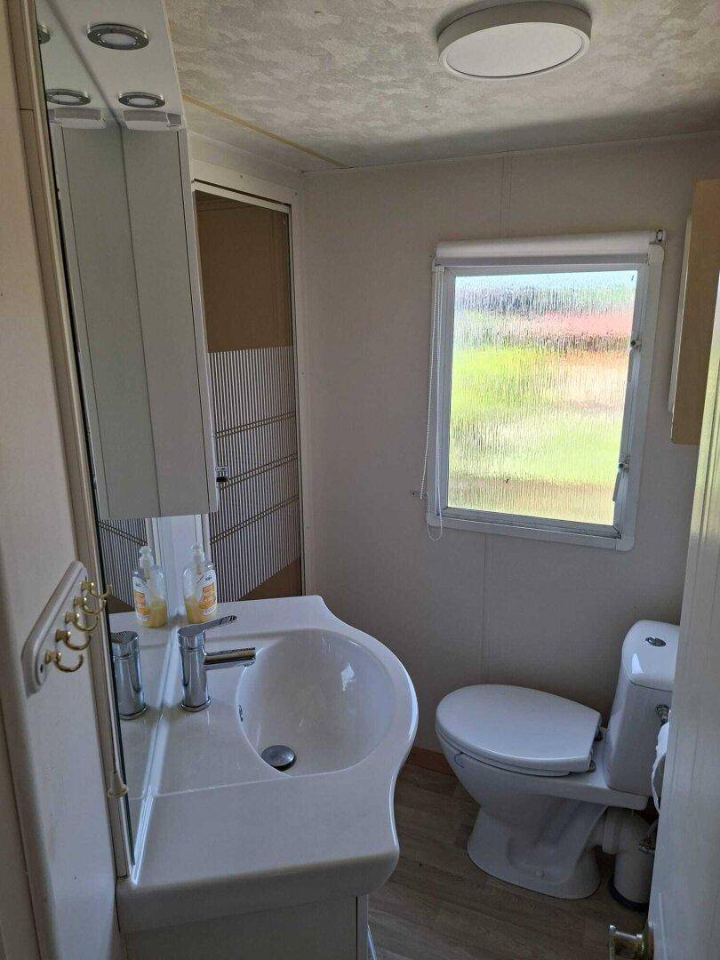 Kleines Badezimmer mit Waschbecken, Toilette, Spiegelschrank und Fenster.