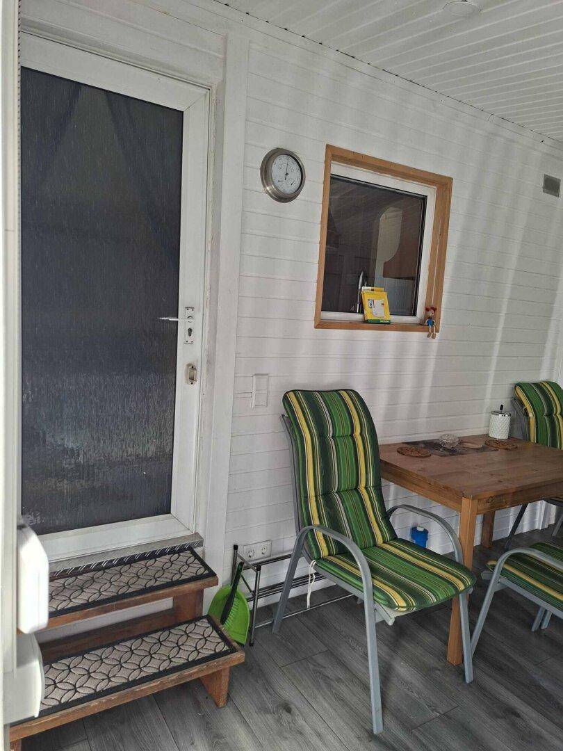 Eingangsbereich des Wintergartens mit Tür, Fenster und Sitzgelegenheiten.