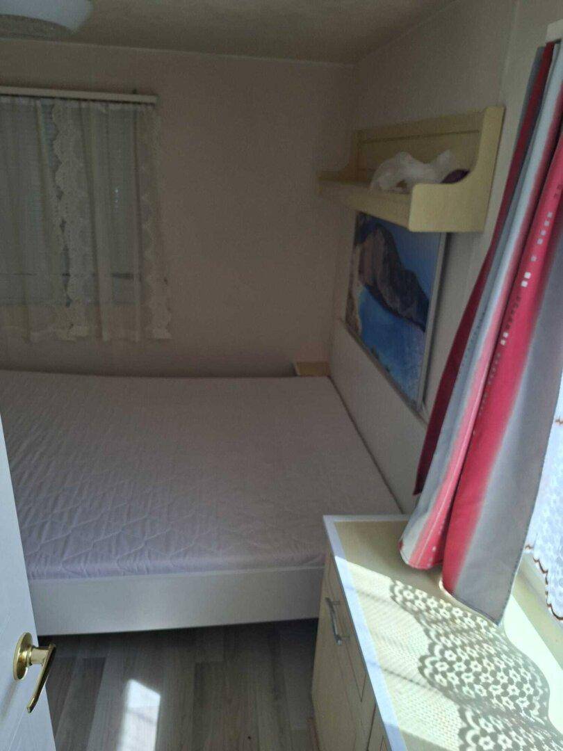 Schlafzimmer mit Einzelbett, Nachttisch und Fenster mit Vorhängen.