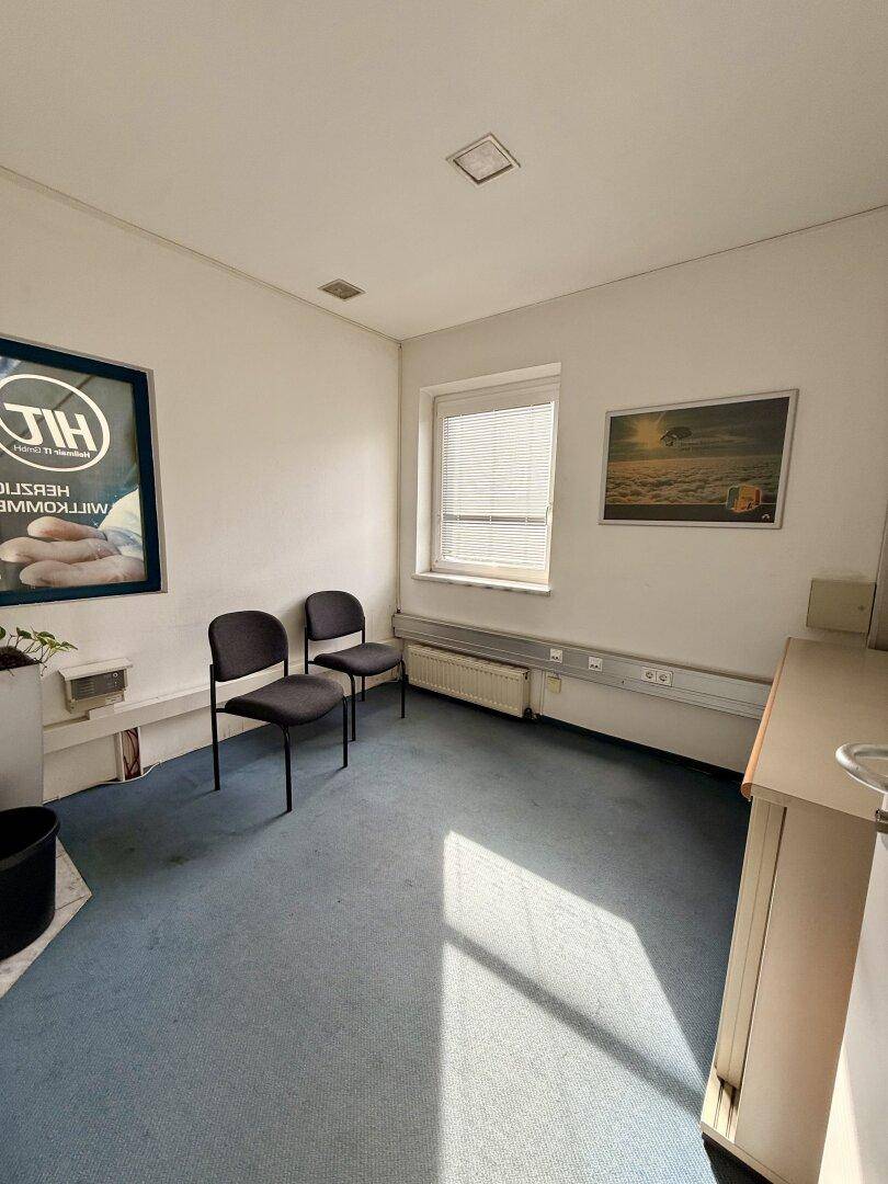 Kleiner Wartebereich oder Büro mit blauem Teppichboden, einem Fenster und zwei Stühlen.