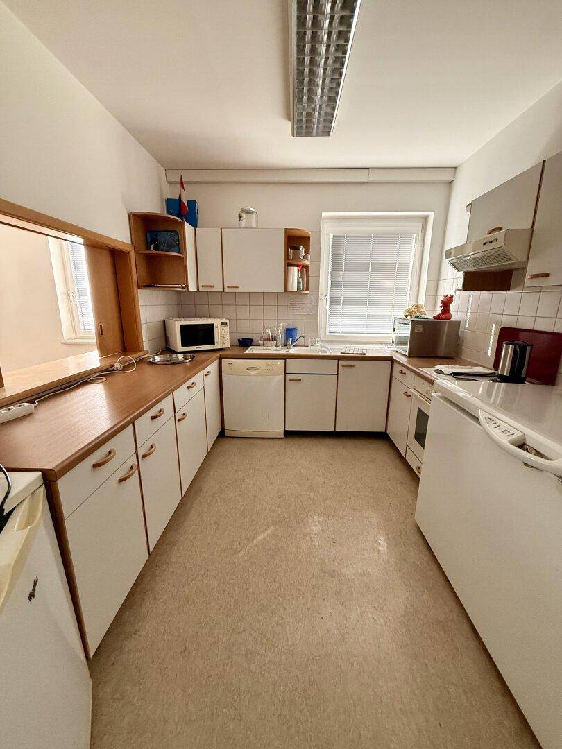 Kleine Küche mit weißen Schränken, Holzarbeitsplatten, einem Fenster und integrierten Geräten.