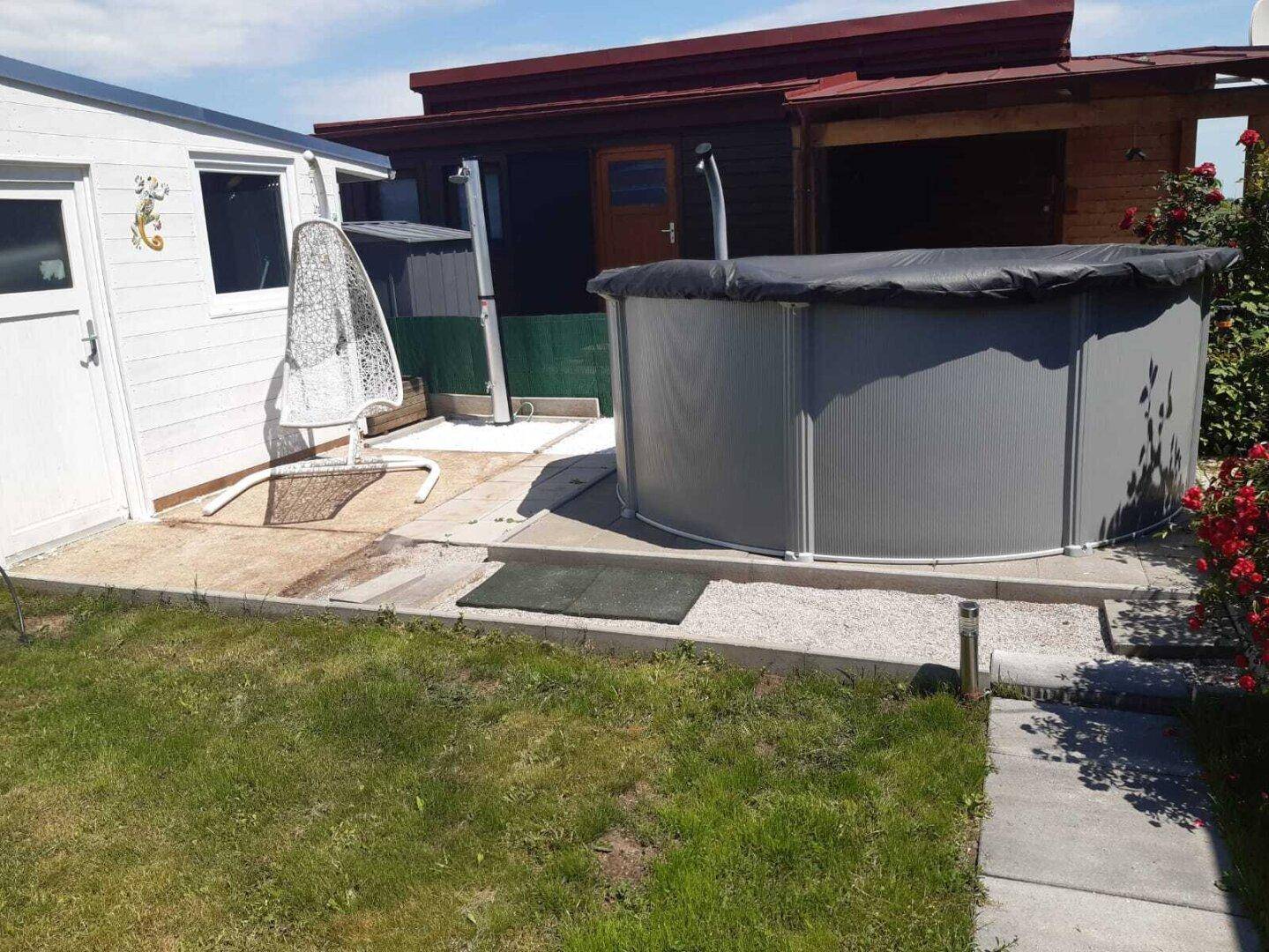 Gartenbereich mit einem Aufstellpool, einer Hängeschaukel und einer kleinen Terrasse.