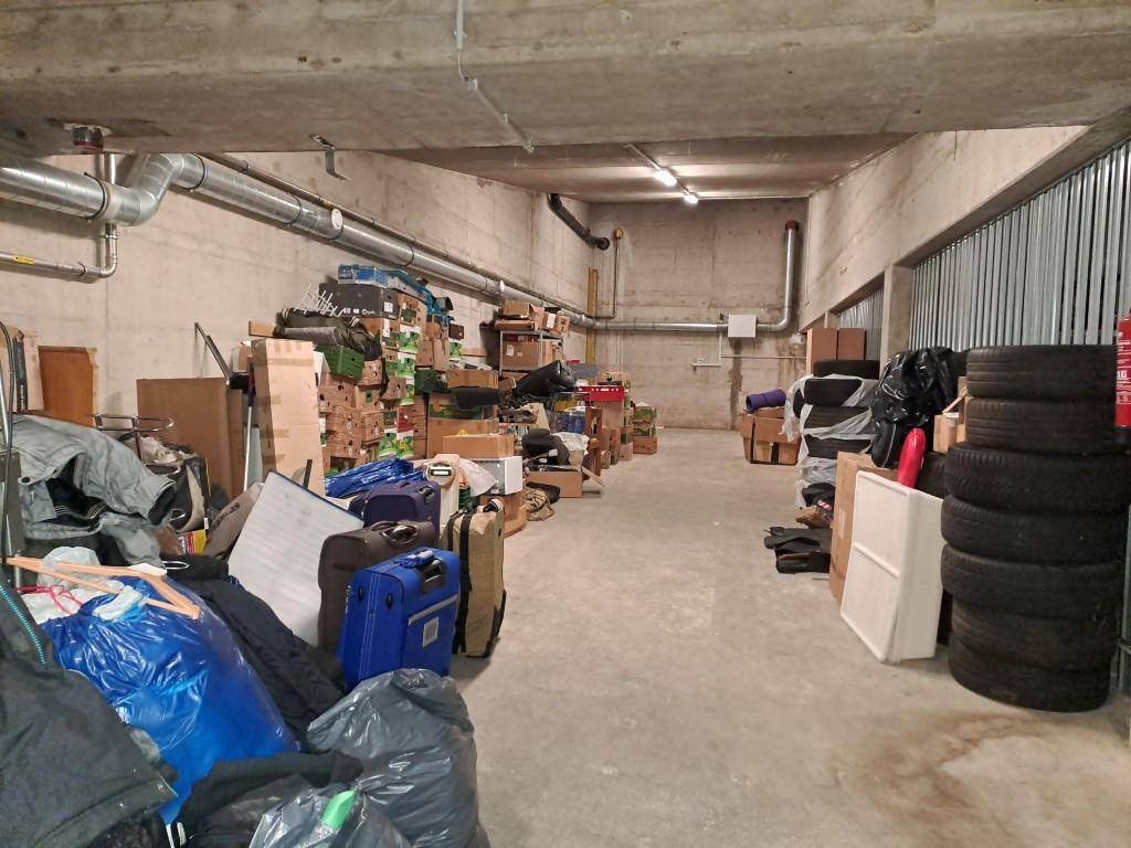 Unaufgeräumter Lagerraum im Keller mit Betonwänden, gefüllt mit verschiedenen Gegenständen und Reifen.