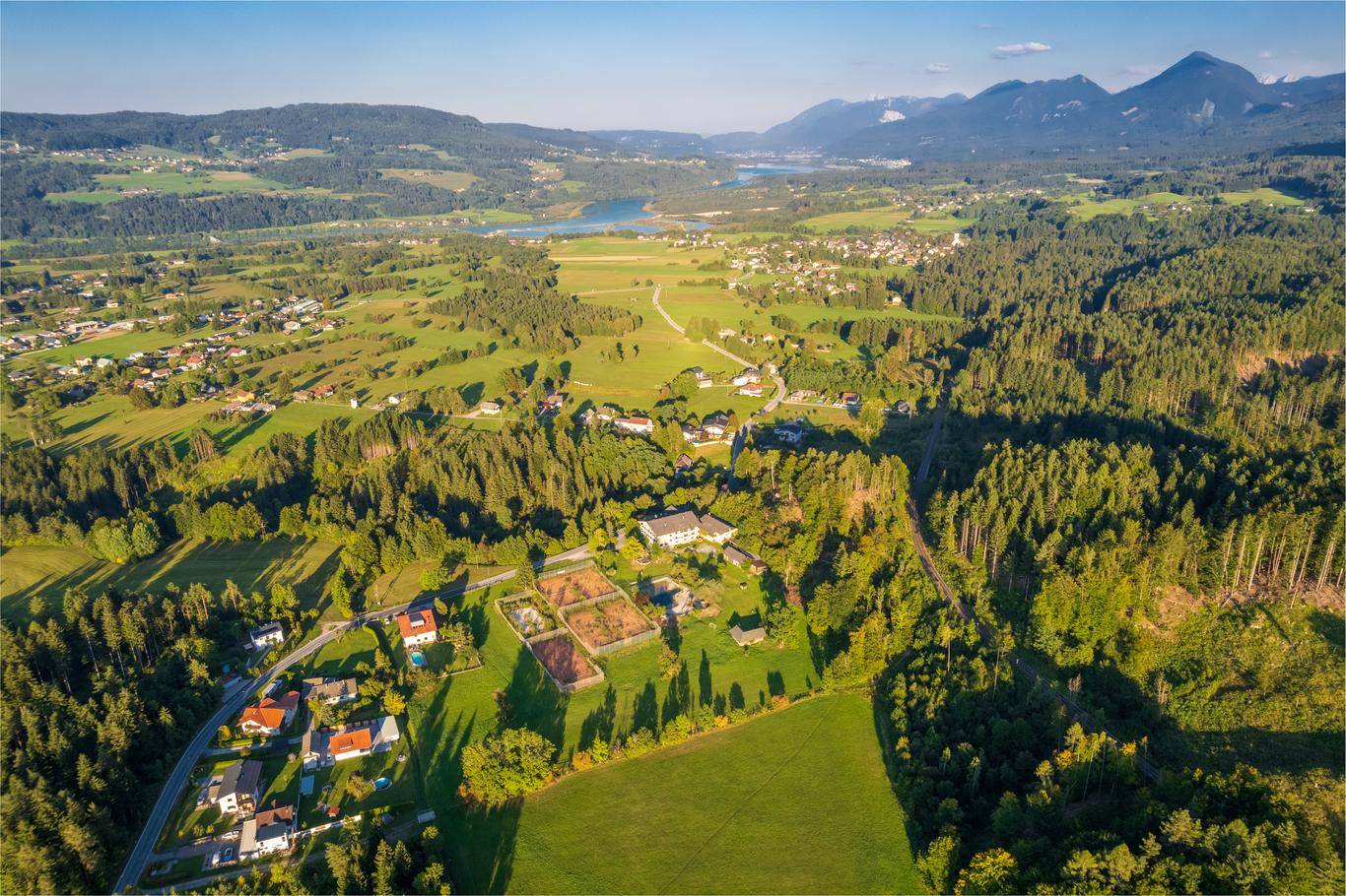 Weitläufige Luftaufnahme einer ländlichen Gegend mit Häusern, Wäldern, Feldern und einem See im Hintergrund.