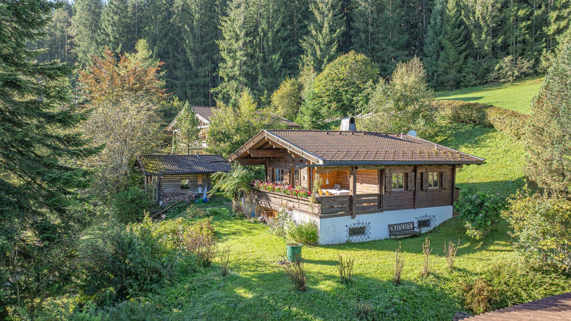 Traditionelles Holzhaus in einer grünen Hügellandschaft, umgeben von Bäumen und Wiesen.
