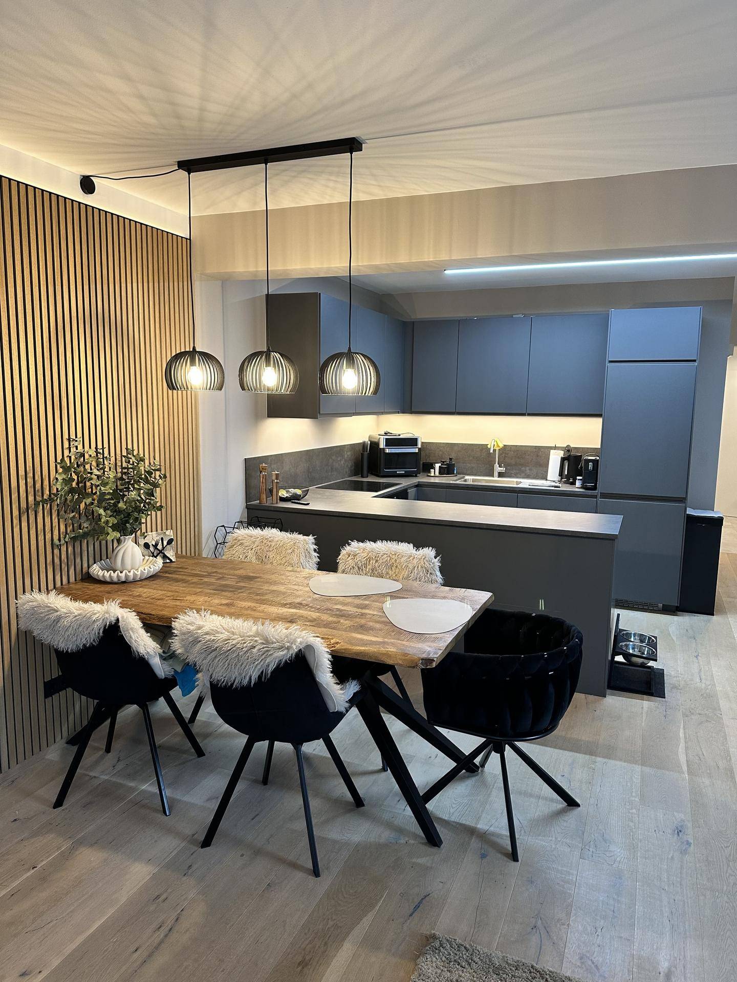 Moderne Küche in Grau mit Essbereich und stilvoller Holzlamellenwand.