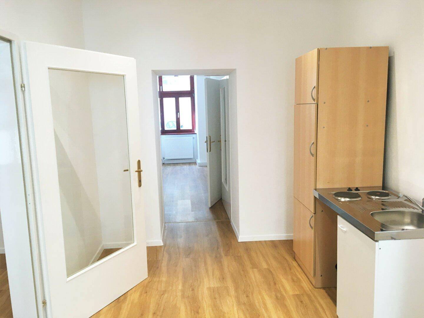 Kleine Küche mit Laminatboden, weißen Wänden und einer einfachen Küchenzeile mit Kochfeld und Spüle.